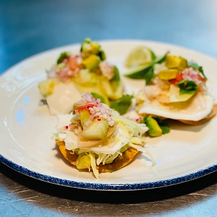 Tostadas topped with fresh ingredients, served with lime wedges on a plate.
