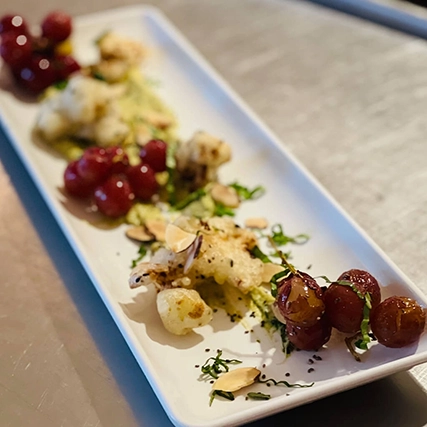 A plate of roasted cauliflower and grapes with almonds.