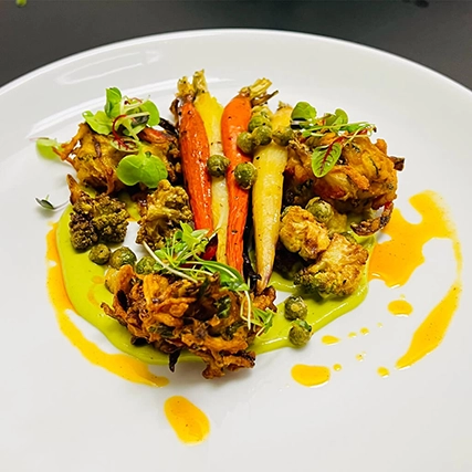 A gourmet meal with roasted vegetables, vegetable fritters, and colorful sauces.