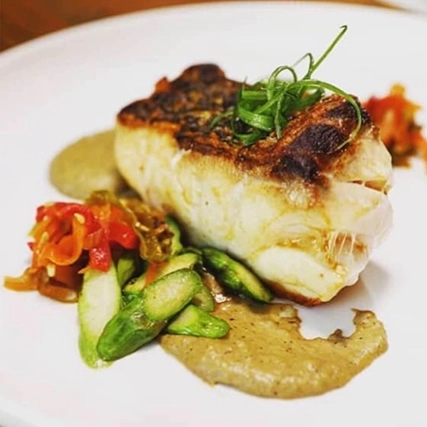 A plated dish featuring seared fish with herbs, a creamy sauce, and sautéed vegetables.