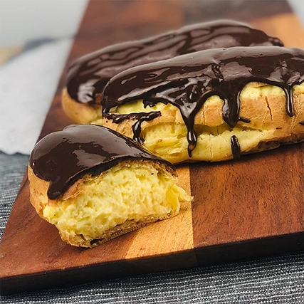 Two chocolate eclairs, one cut open to reveal a creamy yellow filling.