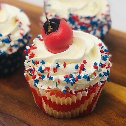 Three decorated cupcakes with colorful sprinkles and a cherry on top of one.