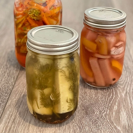 Three jars of preserved vegetables on a wooden surface.