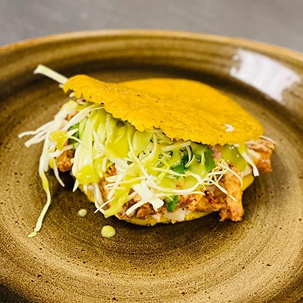 A crispy shell filled with shredded cabbage, green sauce, and seasoned meat on a rustic plate.