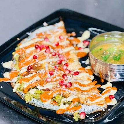 A dosa with vegetable filling, pomegranate seeds, and sauces.