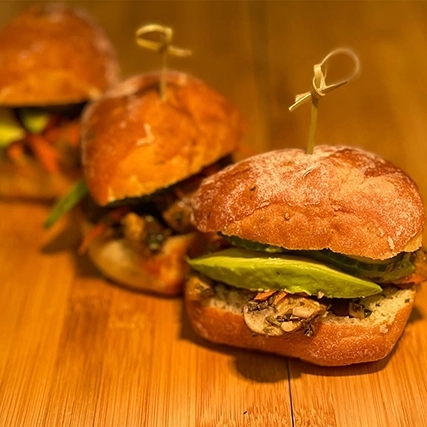 Three sandwiches with avocado slices, mushrooms, and vegetables.