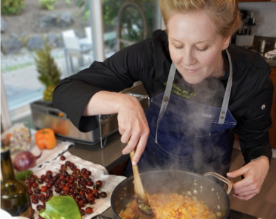 A person cooking in a modern kitchen, stirring a pot of diced vegetables